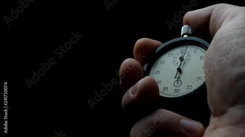 Analogue stopwatch in hand on the black background. Time start with old chronometer. Man presses start button in the sport concept photo