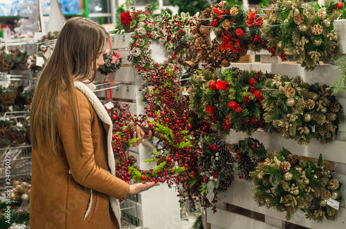 Christmas shopping. Many decorated, christmas wreaths hanging in store for sale. Green Christmas wreath on female hands