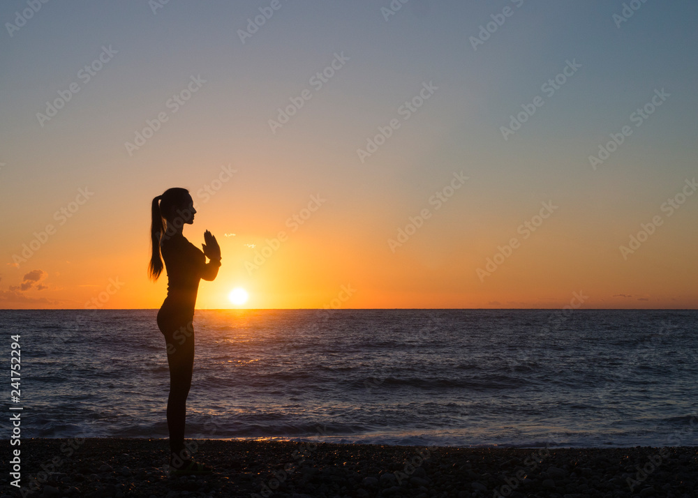 Young woman in a meditating yoga pose overlooking the beautiful sunset. Mind body spirit concept.