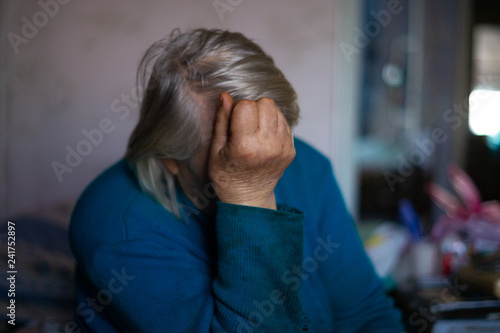 Old poor gray hair woman covered her face with her hand. Woman is sad. Poor life in village. Old age not good. Low-light photo.