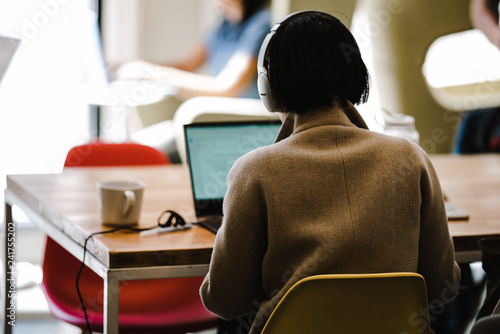 Rear view of woman wearing headphones while using laptop