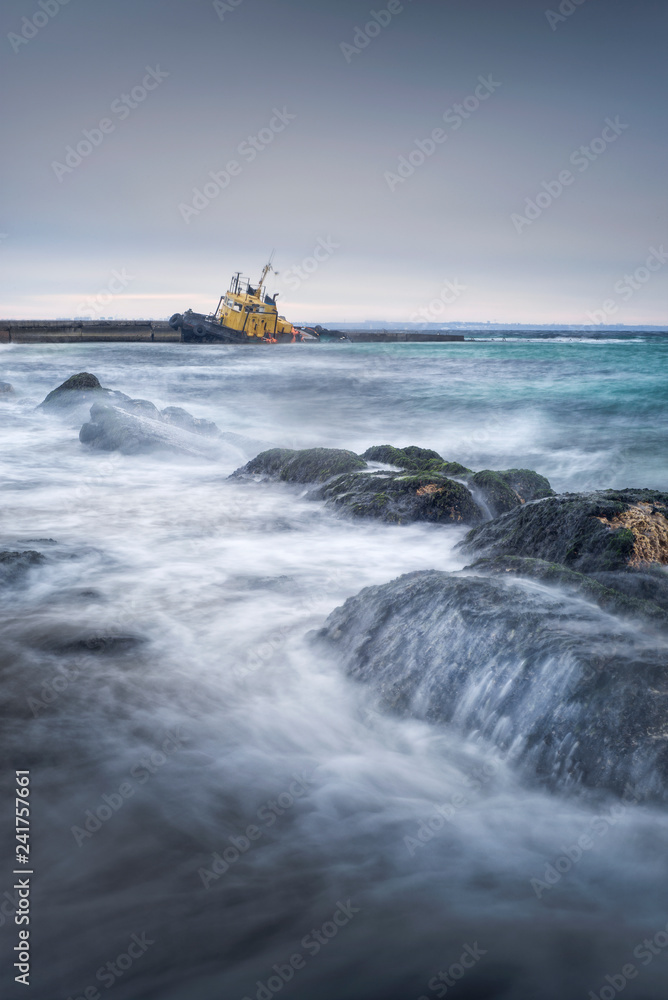 waves on the stones and flooded tug boat 