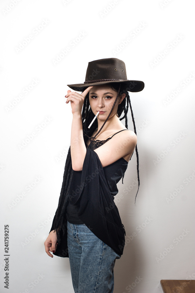 Cute hipster girl wearing a cowboy hat, black top and blue jeans posing on a staircase against a white background. Cute hipster girl wearing a cowboy hat, black top and blue jeans posing on a staircase against a white background.