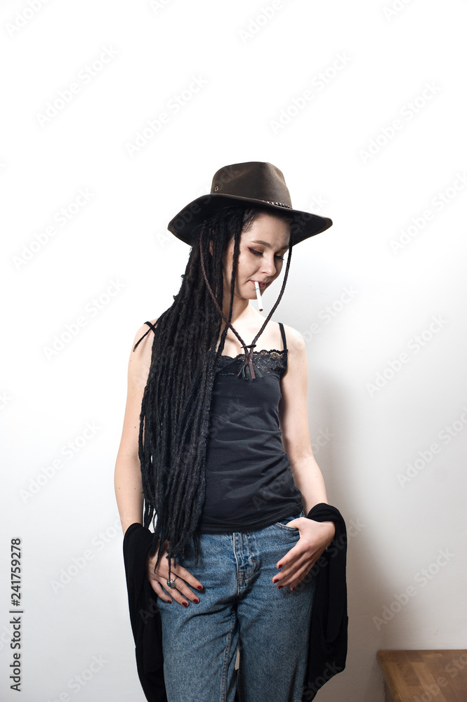 Cute hipster girl wearing a cowboy hat, black top and blue jeans posing on a staircase against a white background. Cute hipster girl wearing a cowboy hat, black top and blue jeans posing on a staircase against a white background.