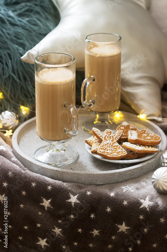 Homemade latte in glass cups, served with gingerbread on the background of plaid, pillows and garlands. photo