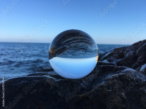 Crystal ball on a wet rock, looking to the sea, sky and horizon. Creative refraction photography