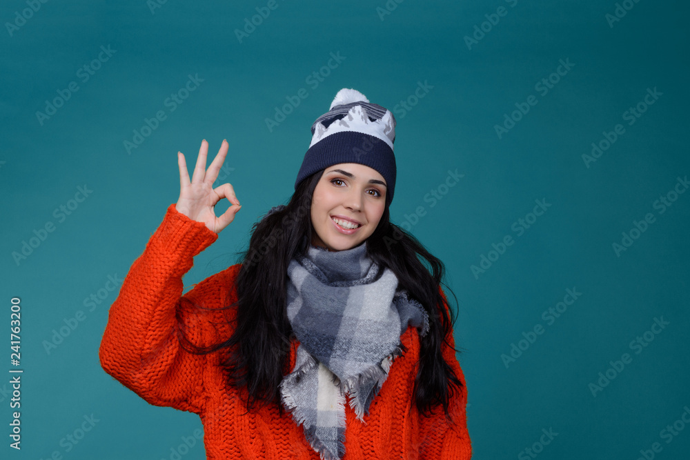 beautiful young smiling brunette woman in checkered gray wool winter hat and scarf smiling . Portrait of beauty winter girl in knitted woolen clothing hat and Snood. Ok sign beautiful young smiling brunette woman in checkered gray wool winter hat and scarf smiling . Portrait of beauty winter girl in knitted woolen clothing hat and Snood. Ok sign