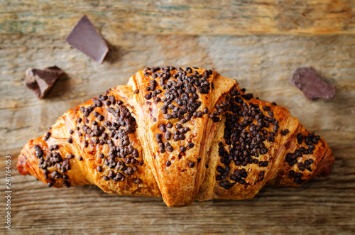 Fresh chocolate croissant with chocolate sprinkles on a wood background