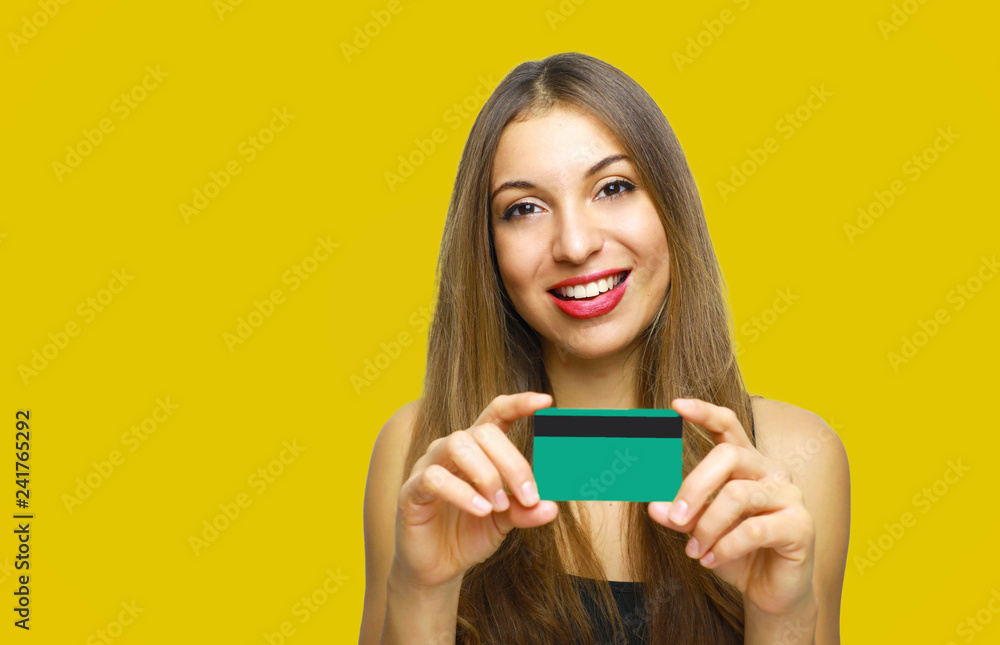 Close up portrait of happy young girl with long hair showing credit card isolated over yellow background Close up portrait of happy young girl with long hair showing credit card isolated over yellow background