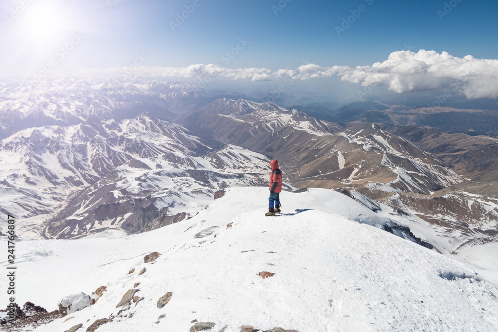 Climber stands at the top of Elbrus 5642m and looks at the mountains
