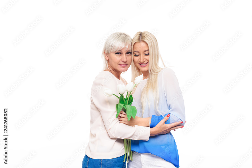 Teen blond daughter and mature mother with bouquet of flowers on white background hugging Teen blond daughter and mature mother with bouquet of flowers on white background hugging
