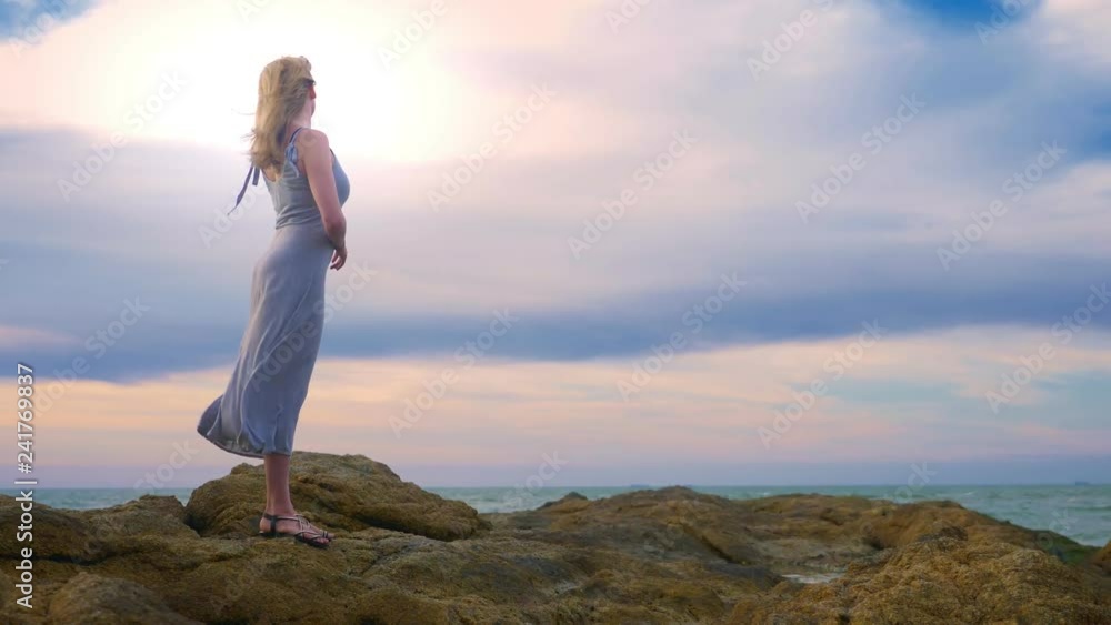 Young woman walking on a rocky and enjoying the view of the sunset, splashing waves Young woman walking on a rocky and enjoying the view of the sunset, splashing waves