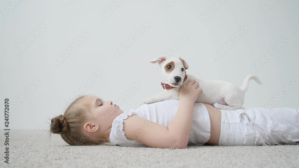 Small girl with the dog playing on the mat at home in white interior Small girl with the dog playing on the mat at home in white interior