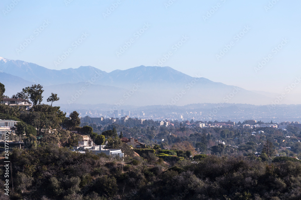 Smoggy morning cityscape view of hillside homes with Hollywood, Los Angeles and the San Gabriel Mountains in background.