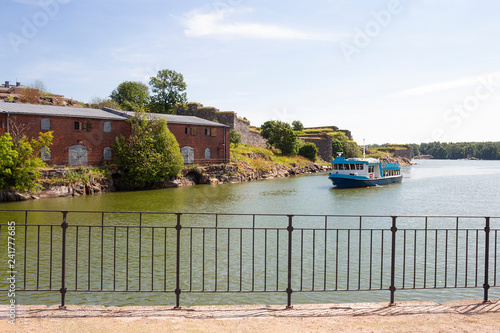 The ferry swims to the pier and the ancient fortifications in the historic island fortress Suomenlinna, Sveaborg in the Gulf of Finland in Finland on a summer day. © NATALIA