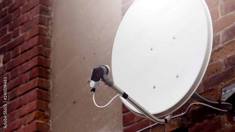 White satellite dish outside on the background of red brick background. Close up of white satellite dish against red brick wall.