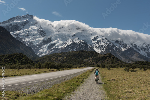Female, baby boomer cyclist cycling on a bike path towards the snow capped and glacier covered Southern Alps, Aoraki/Mount Cook National Park, New Zealand.