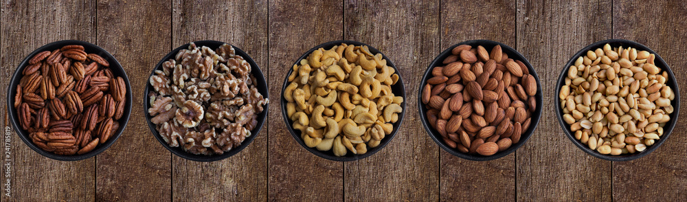 Pekannüsse, Walnüsse, Cashewkerne,Mandelkerne und Erdnüsse in Schüsseln auf Hintergrund aus Holz. Pekannüsse, Walnüsse, Cashewkerne,Mandelkerne und Erdnüsse in Schüsseln auf Hintergrund aus Holz.