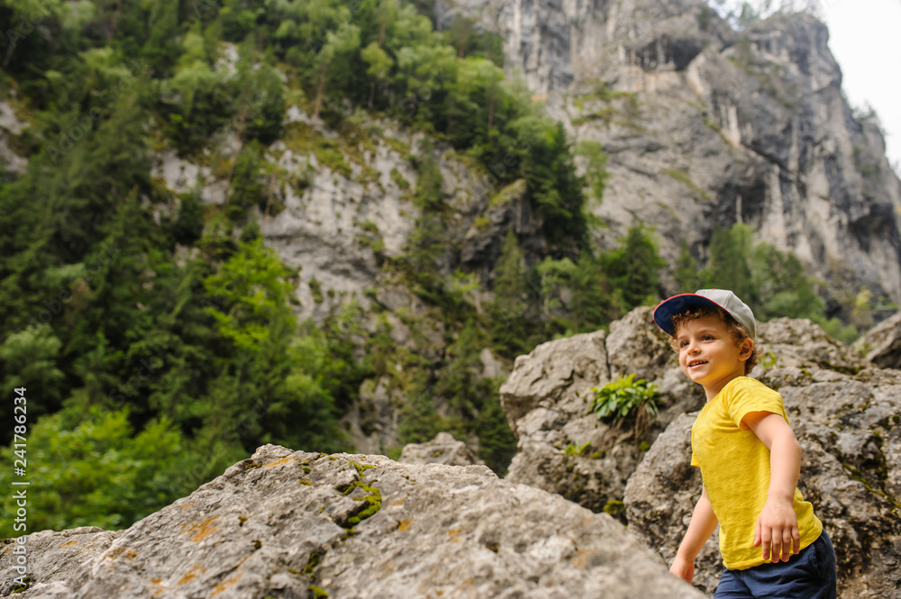 Lateral view of a 6-years blond boy near a rocky mountain surrounded by grass