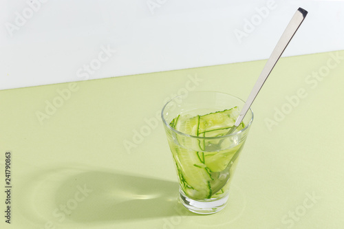 Glass cup with cucumber water on a light green background. Minimalistic creative concept. Copy space.