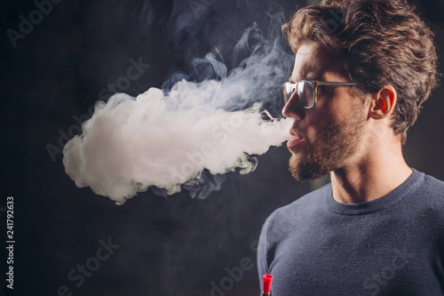 gorgeous man breathing out smoke. close up side view shot. studio shot. bong concept.