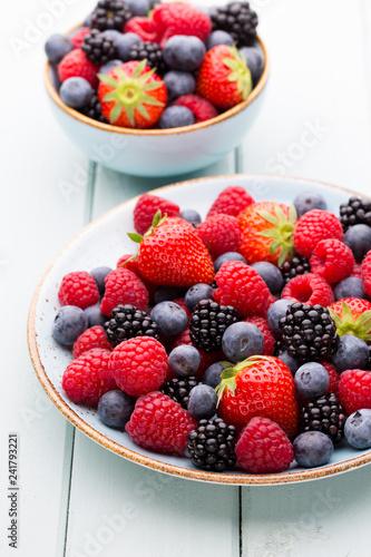 Fresh berry salad on blue dishes. Vintage wooden background.