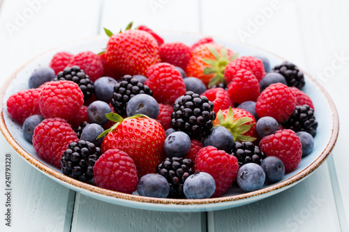 Fresh berry salad on blue dishes. Vintage wooden background.