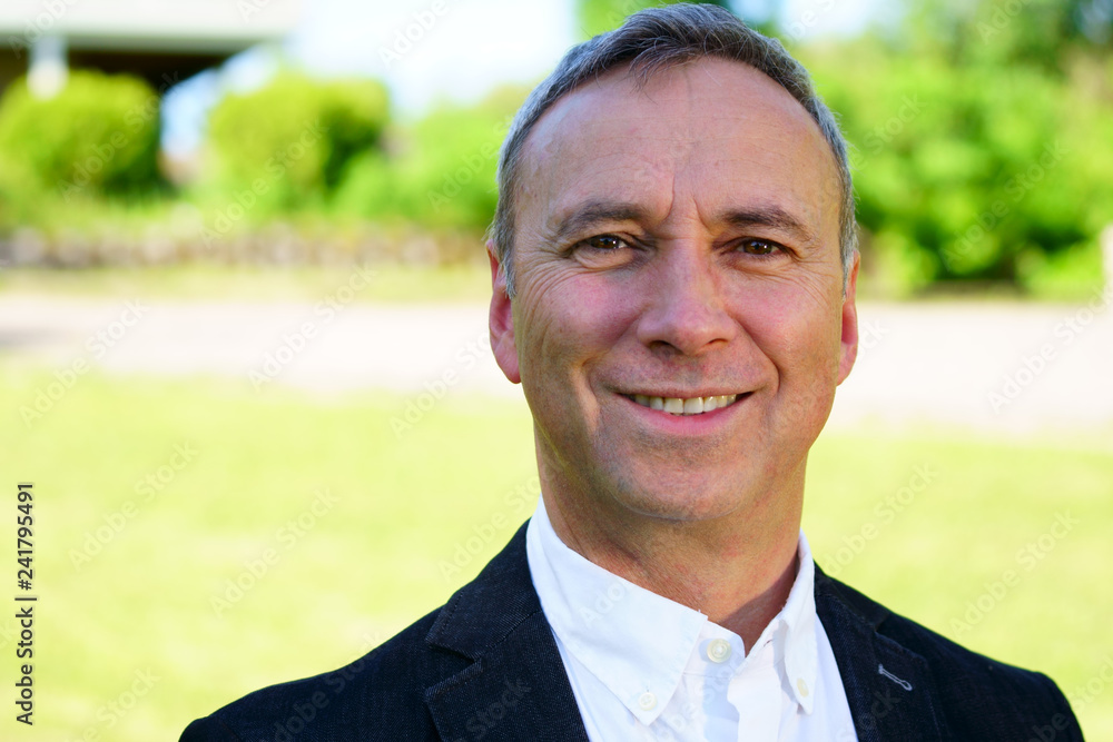 An outdoor portrait of a proud caucasian man wearing a white shirt, a black coat and smiling at the camera. An outdoor portrait of a proud caucasian man wearing a white shirt, a black coat and smiling at the camera.