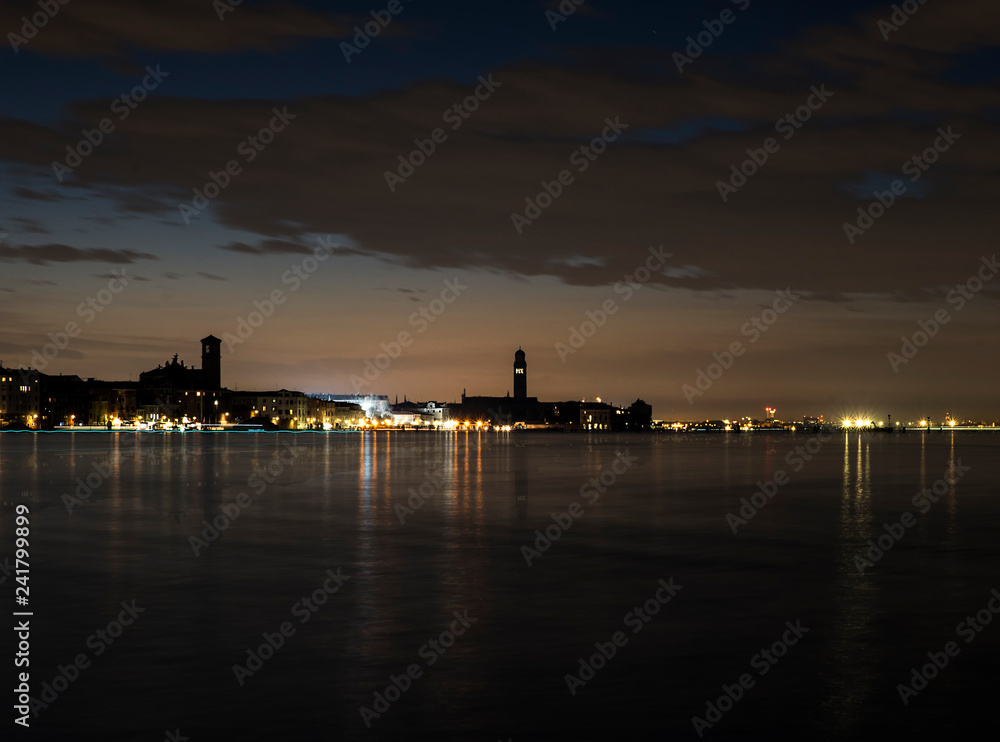 view of Venice at night. The lights of the city are reflected on the water of the lagoon.
