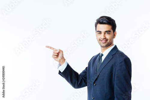 Portrait of a smiling, successful businessman in black suit and tie pointing to side and looking at camera isolated on white background