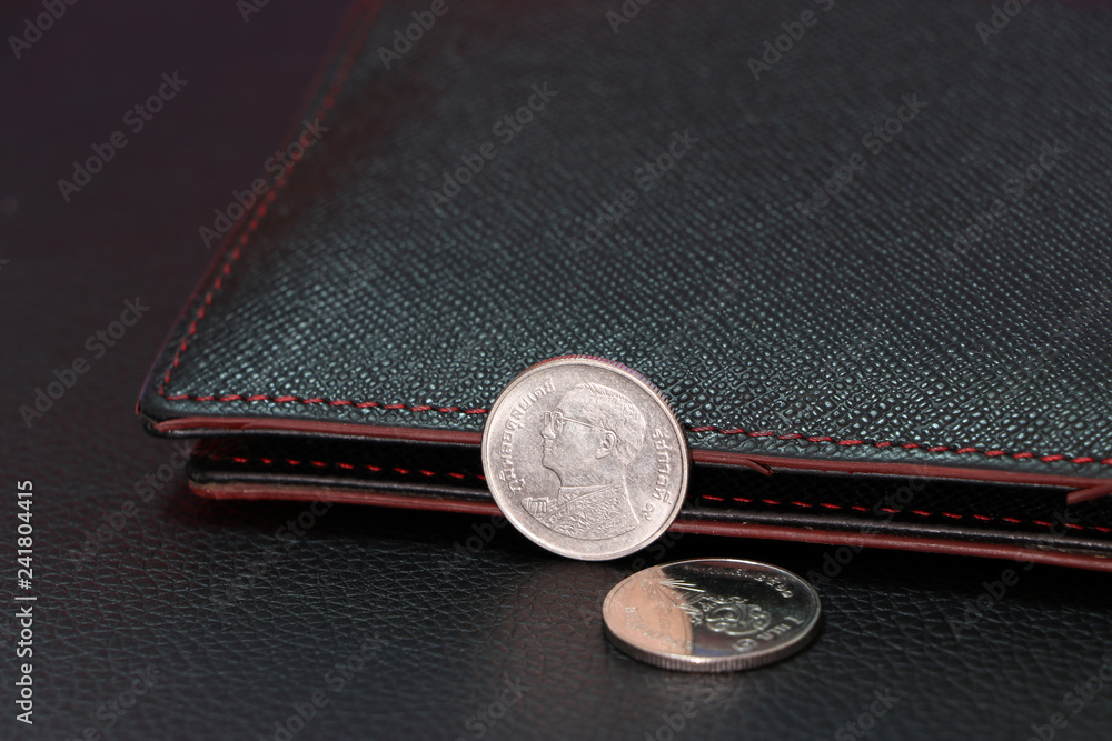Thai one baht coins on obverse (THB) and out focus one baht coins on reverse with black wallet. Thai one baht coins on obverse (THB) and out focus one baht coins on reverse with black wallet.