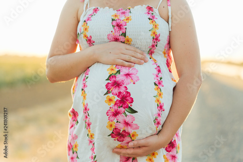 Closeup of a pregnant young woman in a floral dress outdoors. 