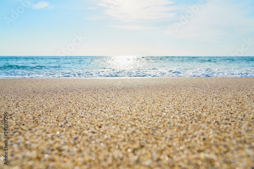 Sandy beach with waves and foam as a natural background with reflection of sunlight on water. Summer holiday concept.