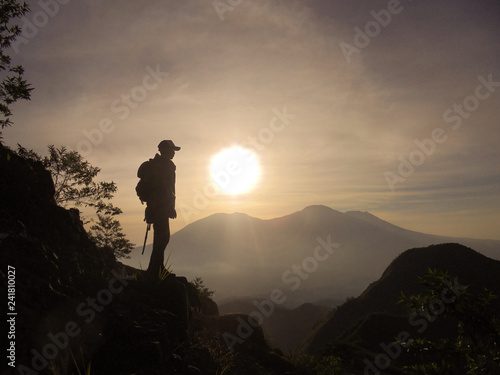 Silhouette of Hiker man standing on hill during sunrise in the morning with views of mountain