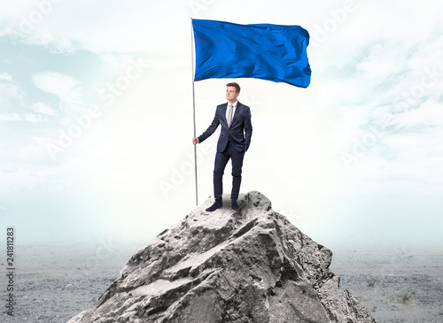 Handsome businessman on the top of the mountain with blue flag 