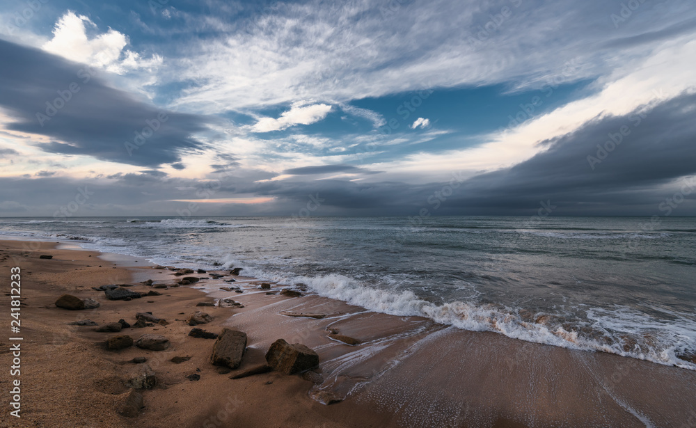Seashore, stormy sea and colorful clouds on the horizon