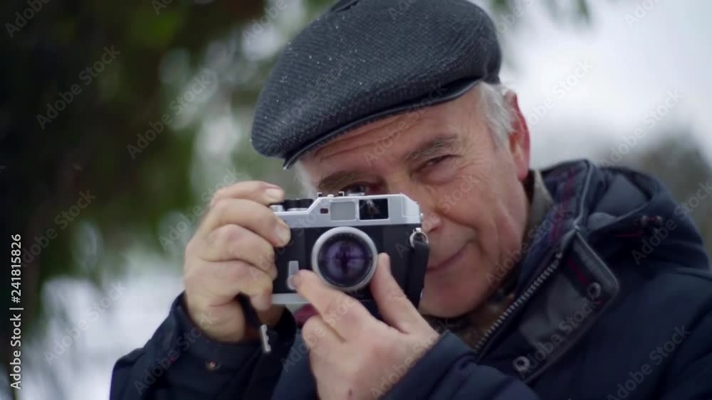 elderly male retiree is viewing through lens of old photo camera outdoors in winter day elderly male retiree is viewing through lens of old photo camera outdoors in winter day