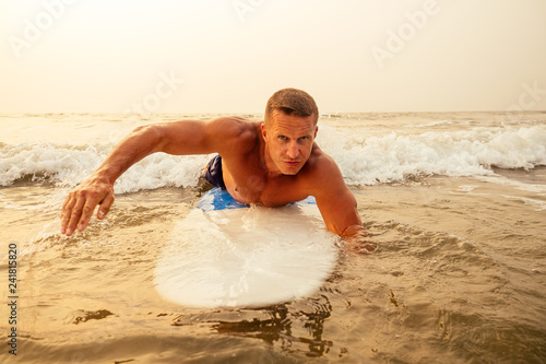 surfing freelancing man muscle and press sport training on the beach at sunset.male fitness model surfer with a big surf board near the indian ocean goa Ashwem Arambol beach photo