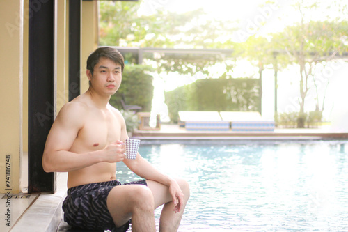 asian man holding cup of coffee on the edge of a swimming pool © Nattapol