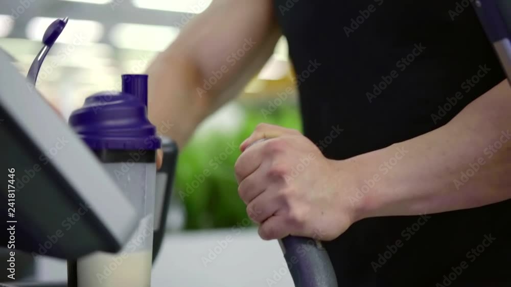 muscular sportsman is working out on elliptical trainer, listening to music by headphones muscular sportsman is working out on elliptical trainer, listening to music by headphones
