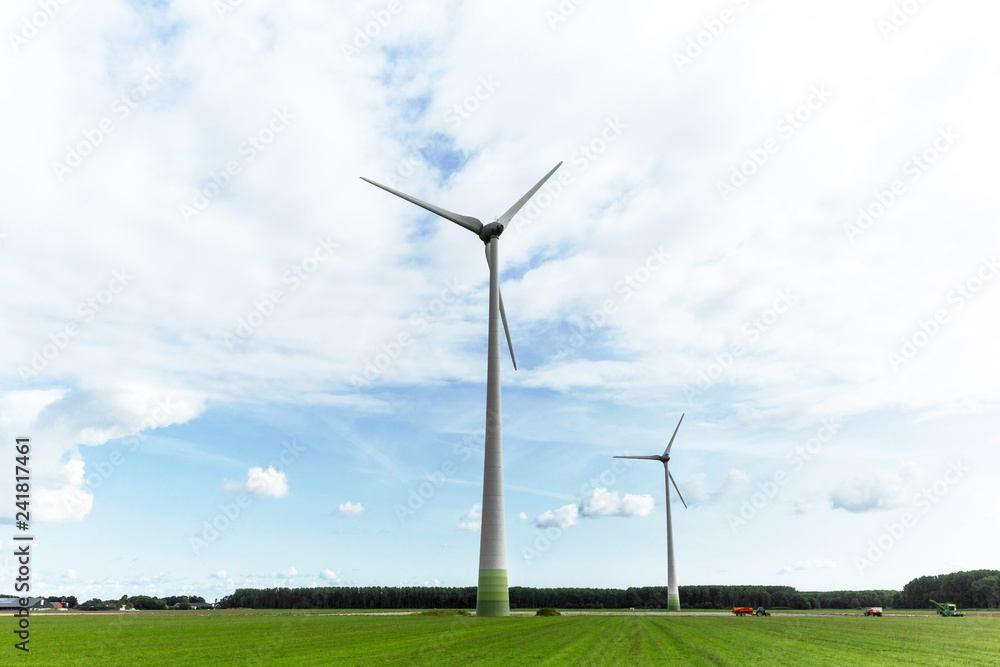 Lelystad, The Netherlands - August 31, 2018: Wind turbines standing tall in the dutch countryside generating sustainable energy for the future. You can see how the farms have become so accustom to the Lelystad, The Netherlands - August 31, 2018: Wind turbines standing tall in the dutch countryside generating sustainable energy for the future. You can see how the farms have become so accustom to the