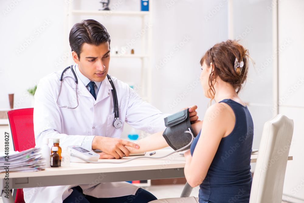Fototapeta premium Young doctor checking woman's blood pressure