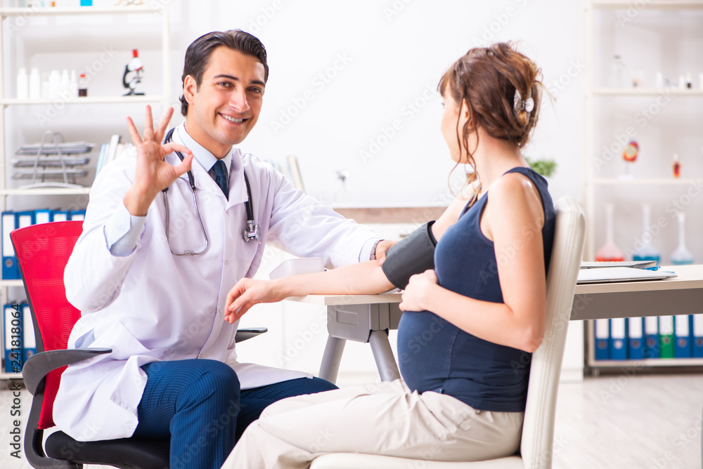 Fototapeta premium Young doctor checking pregnant woman's blood pressure