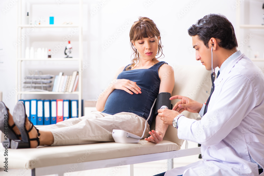 Fototapeta premium Young doctor checking pregnant woman's blood pressure