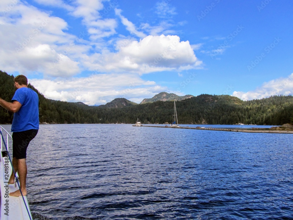 A man preparing to dock his boat at a dock on Alexander Island, on Gambier Island, in Howe Sound, British Columbia, Canada.  A beautiful summer day with calm waters and beautiful blue skies.