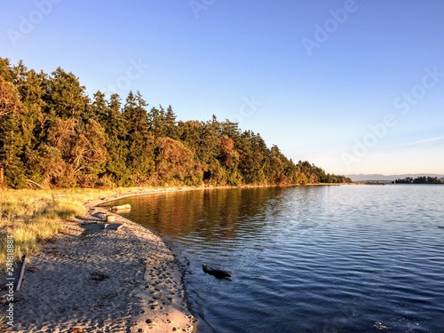 A beautiful secluded sandy beach on Sidney Island in the Gulf Islands of British Columbia, Canada.  The ocean water is calm on a gorgeous evening as the sun begins to set. © christopher