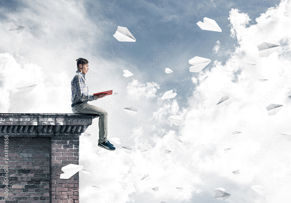 Handsome student guy on roof edge reading book and paper planes Handsome student guy on roof edge reading book and paper planes