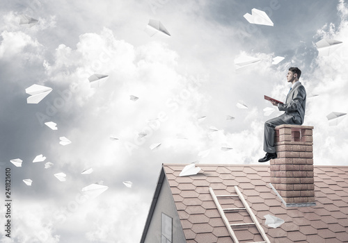 Man on brick roof reading book and paper planes flying in air