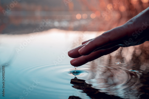 Finger touches surface of mountain lake. Hand reflection