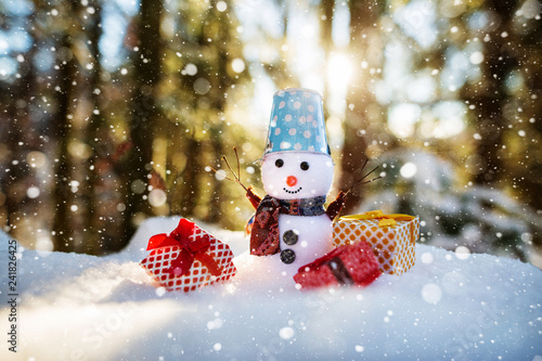 Happy snowman with gift boxes standing in winter christmas landscape. Snowman smiling standing in snow near spruce trees